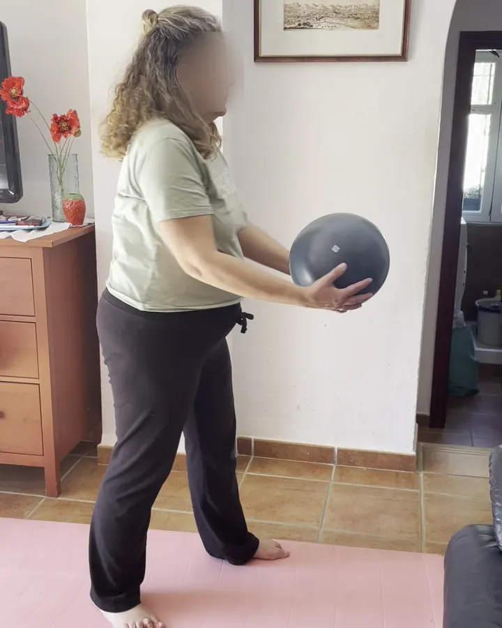 Clienta entrenando con un balón medicinal en el hueco entre una cómoda y la pared, en su casa de Málaga