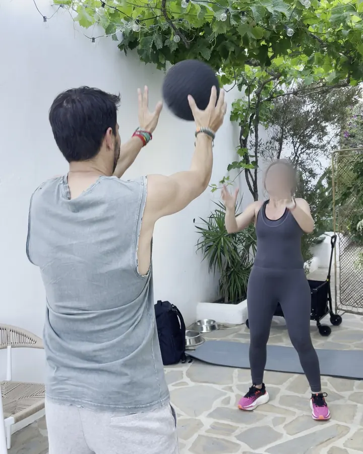 Pareja entrenando con un balón medicinal en el patio de su casa, en Málaga