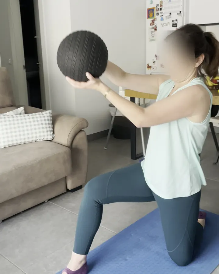 Clienta entrenando con un balón medicinal en el salón de su casa, en Málaga
