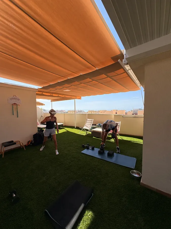 Una pareja entrenando en la terraza de su casa bajo el toldo